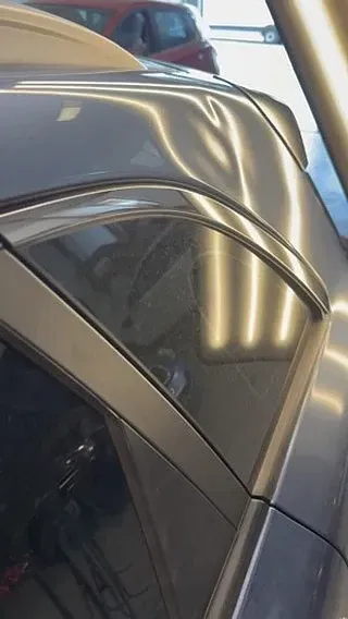 Un coche plateado con el techo dañado está aparcado en un garaje.