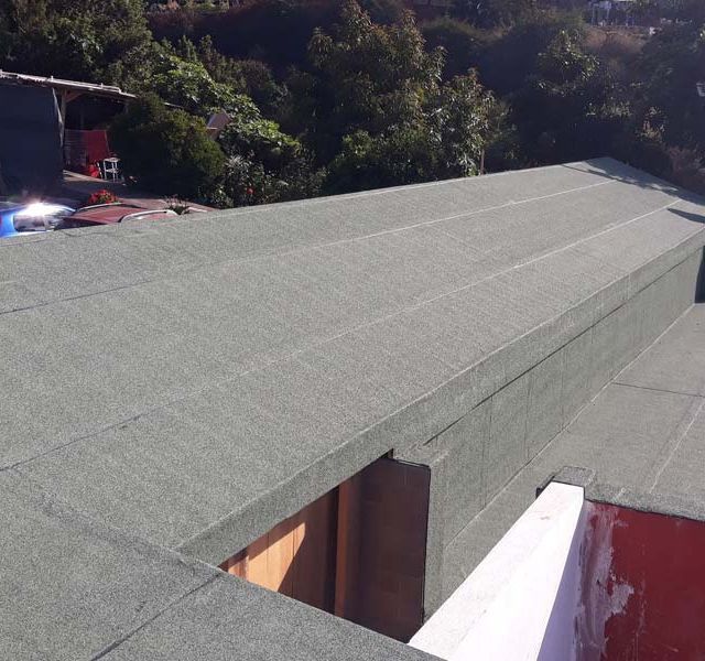 Un tejado con techo verde y árboles al fondo.