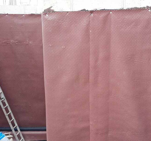 Una escalera está junto a un gran trozo de tela marrón en una pared.