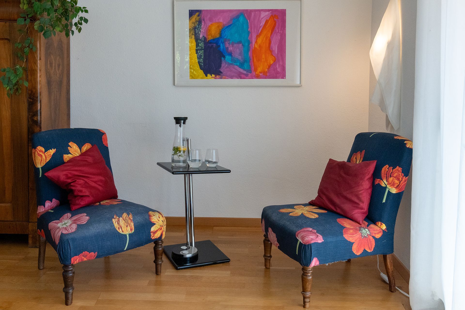 Zwei Stühle stehen neben einem Tisch in einem Raum mit einem Gemälde an der Wand.