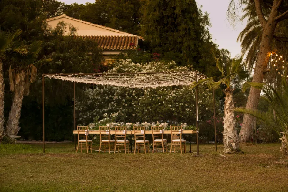 Mesa de banquete al aire libre bajo un toldo blanco en un jardín cubierto de césped al atardecer.