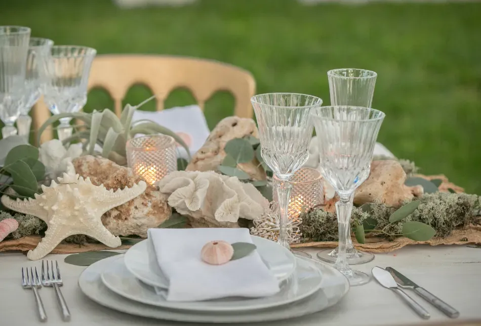Elegante mesa puesta con platos dorados, copas verdes y servilletas enrolladas de color amarillo pálido sobre un mantel floral.