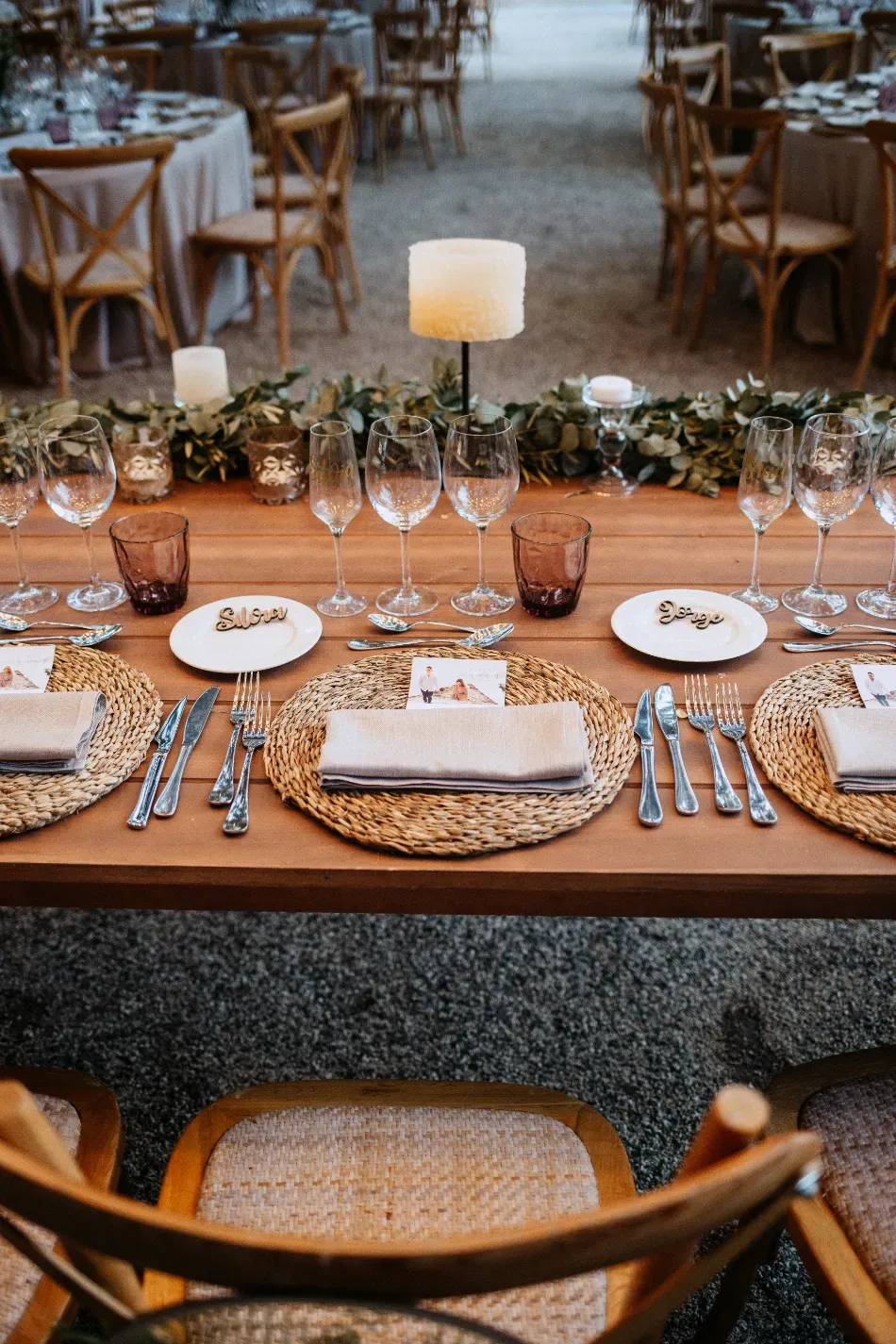 Elegante conjunto de mesa y sillas de mimbre para comer al aire libre, velas, cristalería y platos blancos listos para recibir a los invitados.
