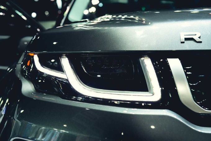 Primer plano de la parrilla delantera de un coche oscuro con faros LED blancos brillantes y un emblema R.