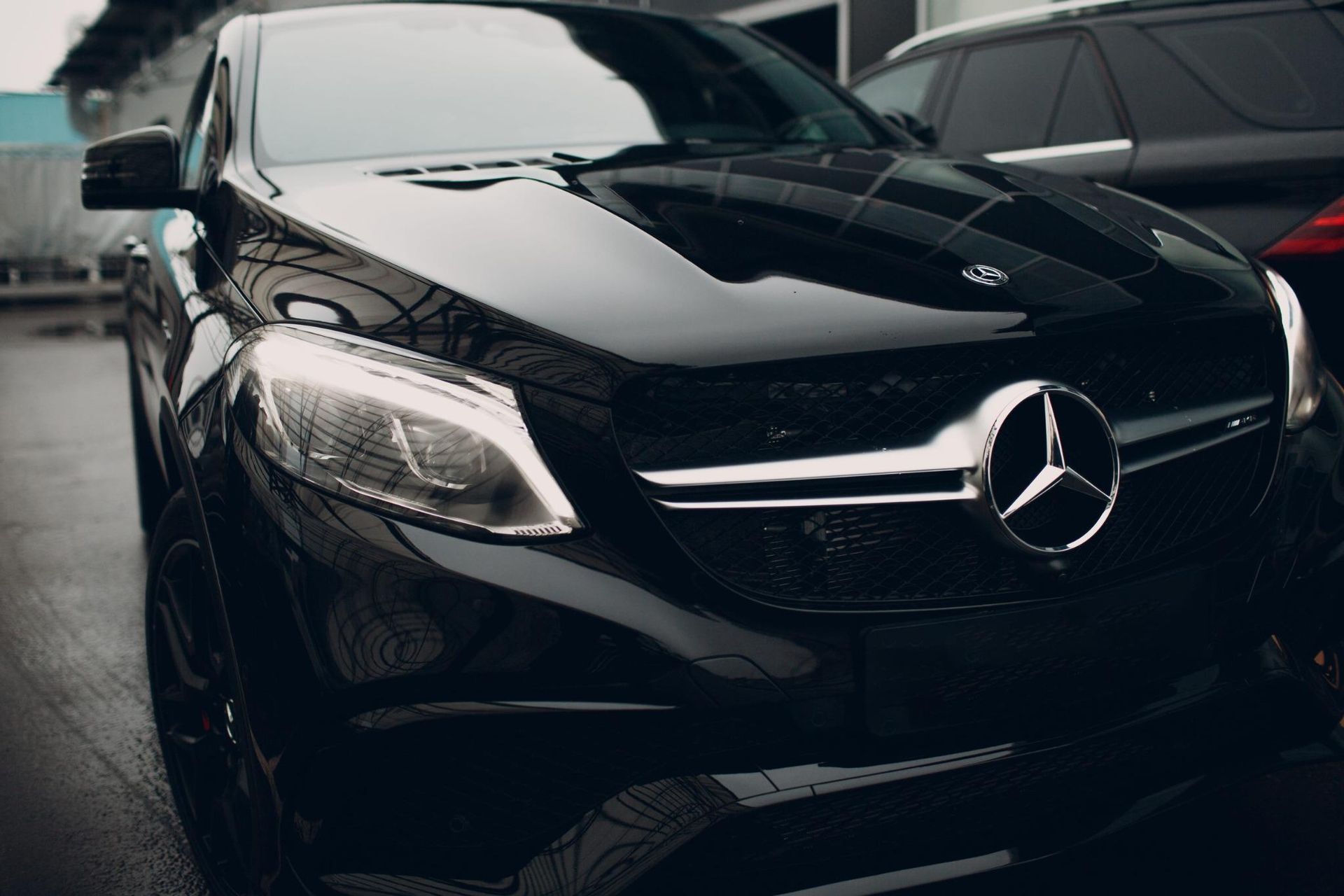 Vista frontal de un Mercedes-Benz negro en un estacionamiento, con un coche rojo detrás.