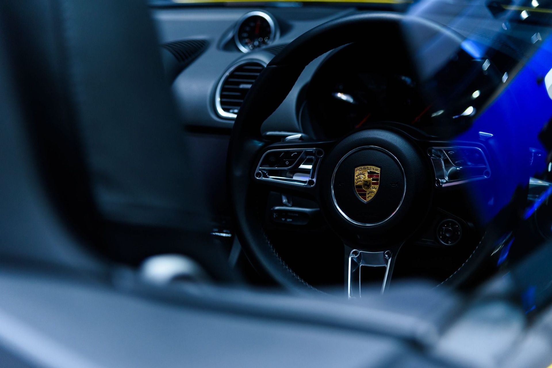 Interior de un lujoso coche deportivo con volante Porsche y reflejos azules en el salpicadero.