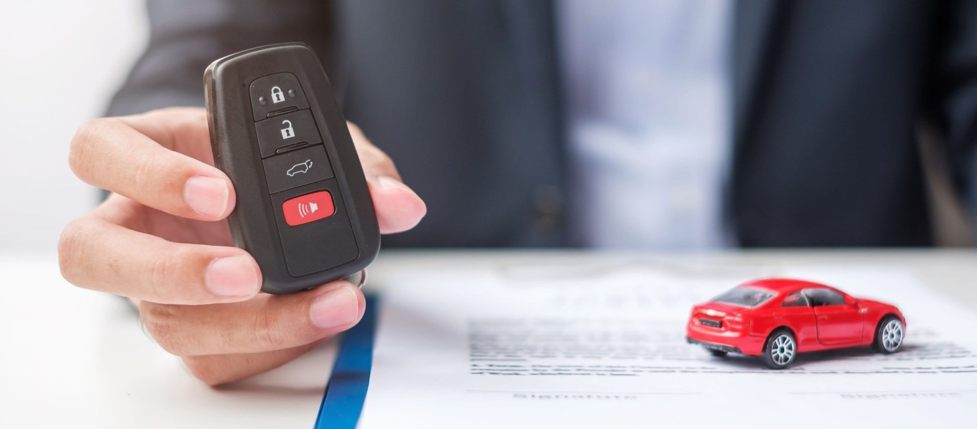 Una mano sostiene el llavero del coche junto a un coche de juguete rojo en la documentación del seguro.