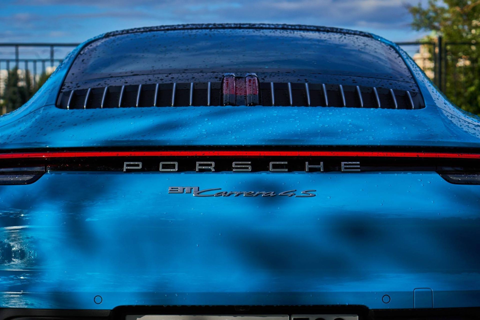 Vista trasera de un Porsche 911 Turbo S azul con tira de luces traseras rojas y ventana trasera tintada.