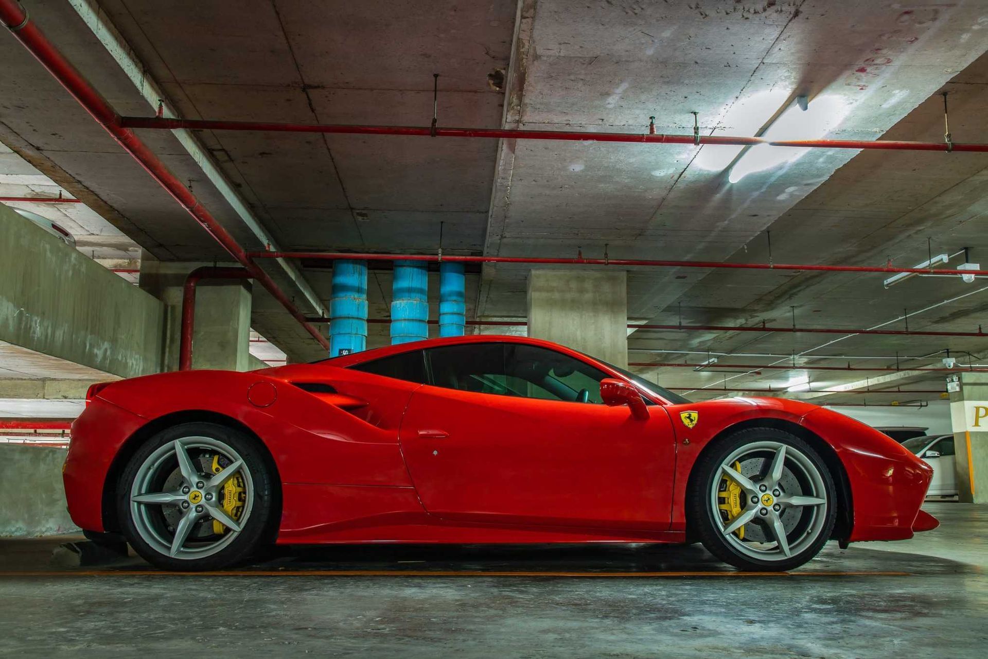 Coche deportivo rojo aparcado en un garaje de hormigón, vista lateral.