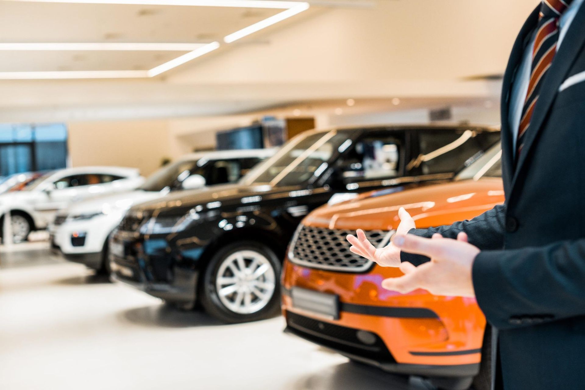Un vendedor con traje sostiene las llaves de un coche en una luminosa sala de exposición con coches.