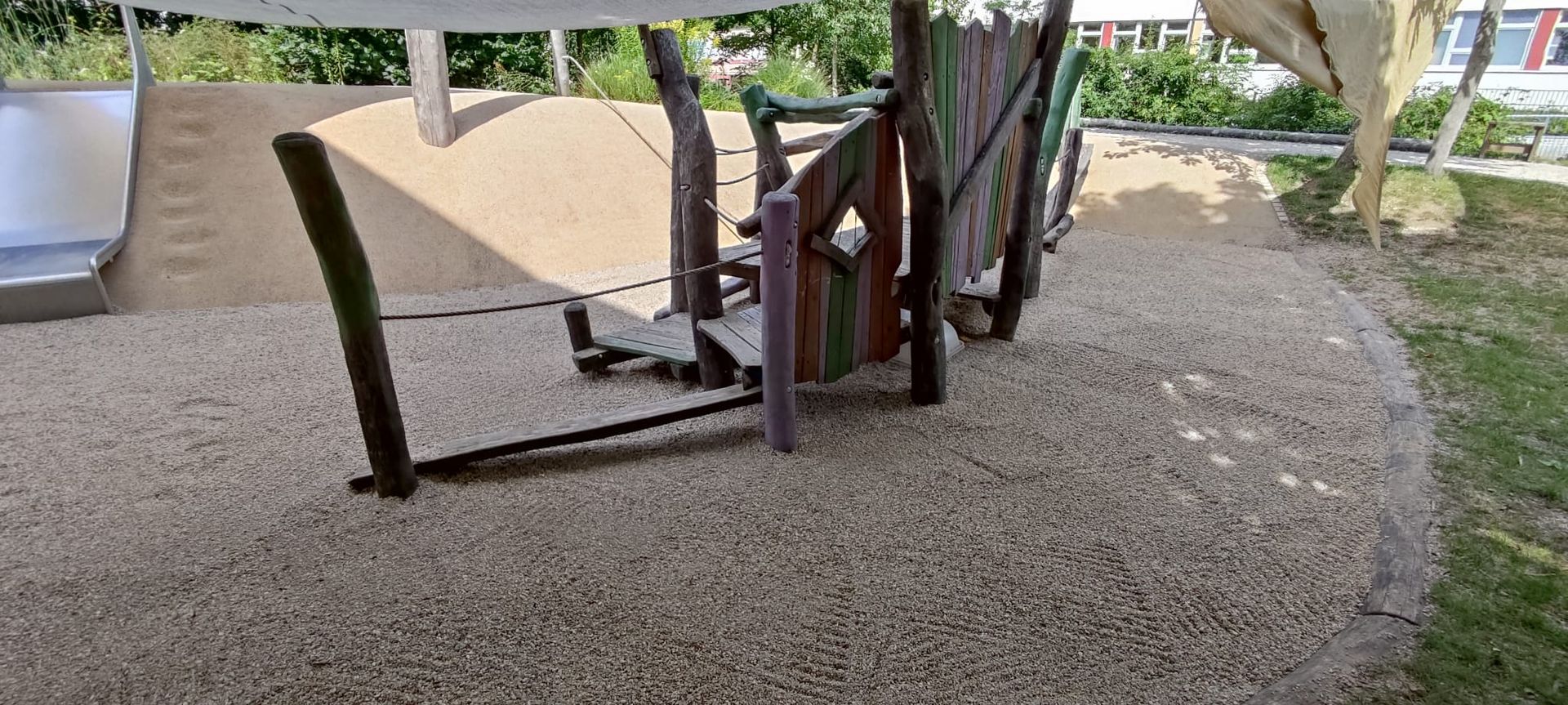 Ein Kinderspielplatz mit Rutsche und Holzspielgerät auf einem Kiesbett.