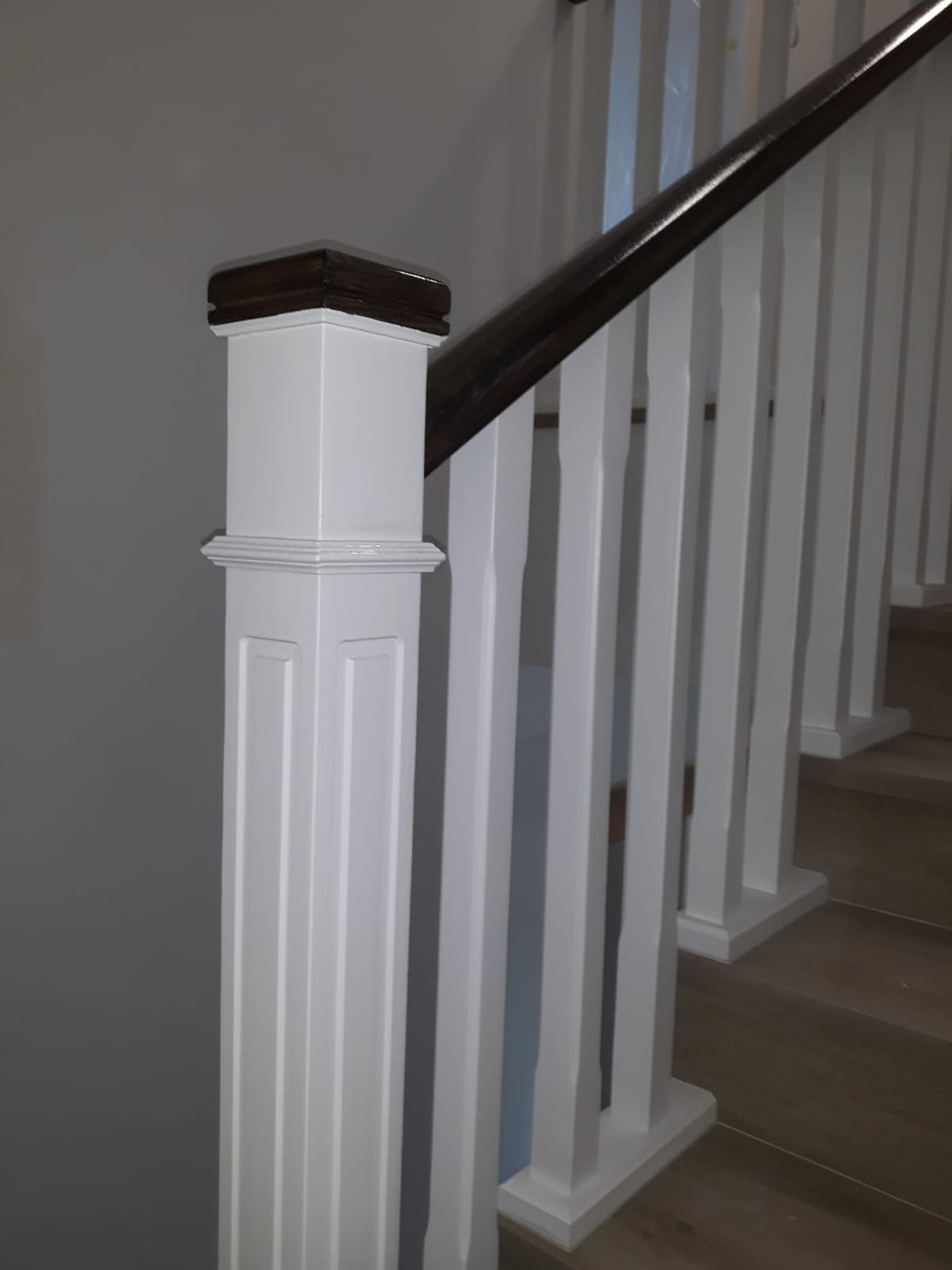 Un primer plano de una barandilla blanca con pasamanos de madera en una escalera.