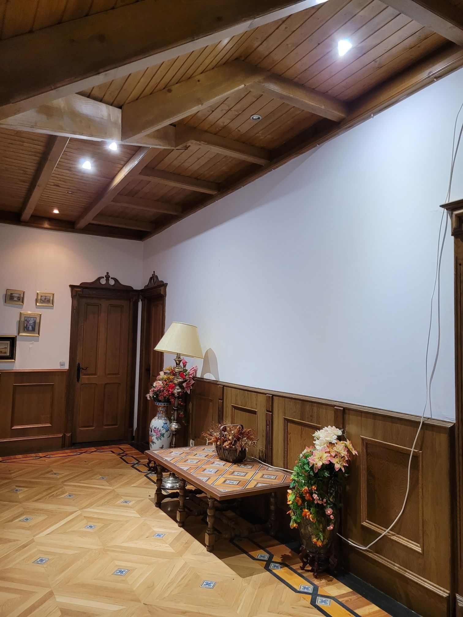 Un pasillo con paneles de madera, una mesa, una lámpara y un jarrón con flores.