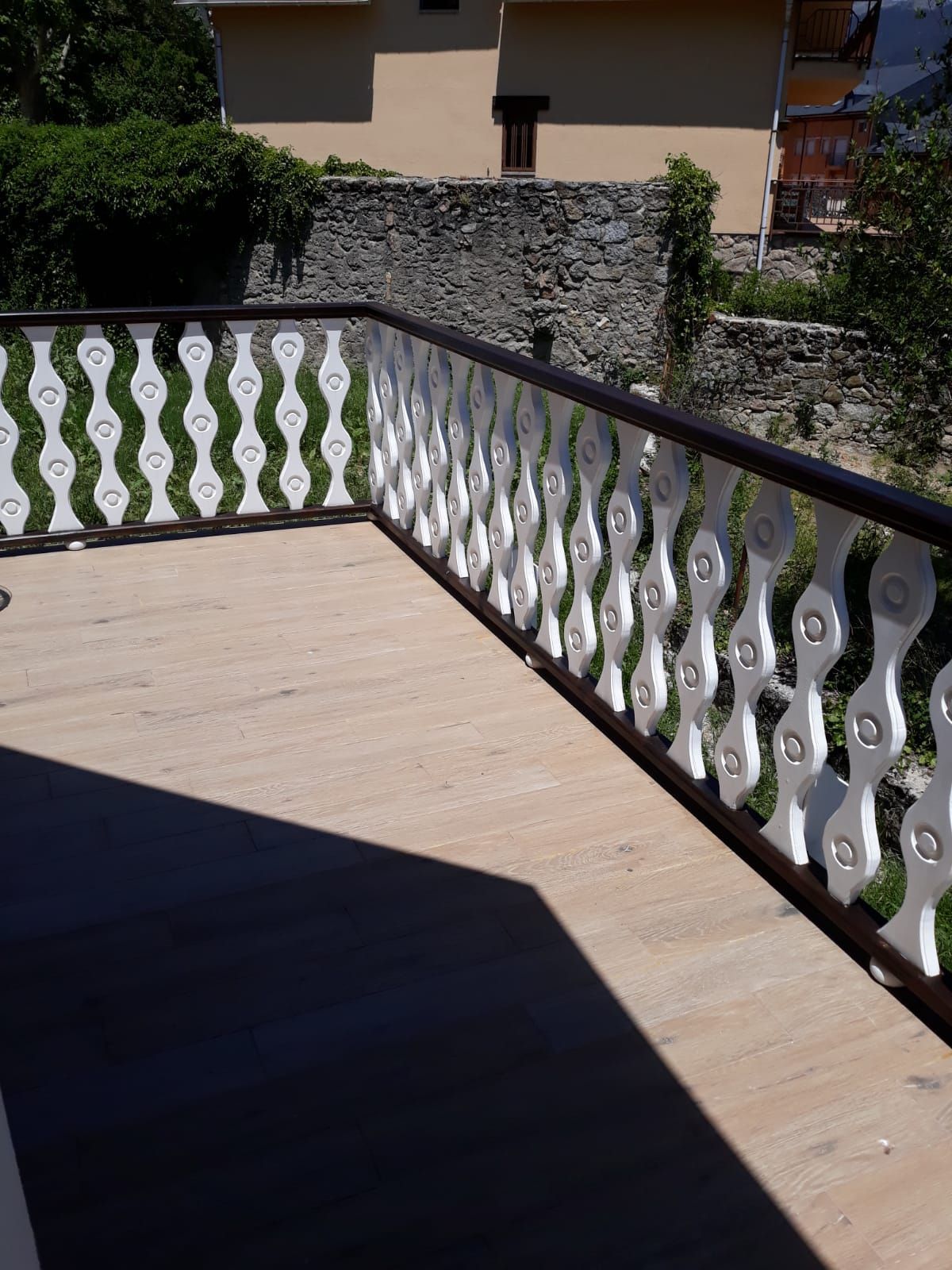 Un balcón con barandilla blanca y un muro de piedra al fondo.