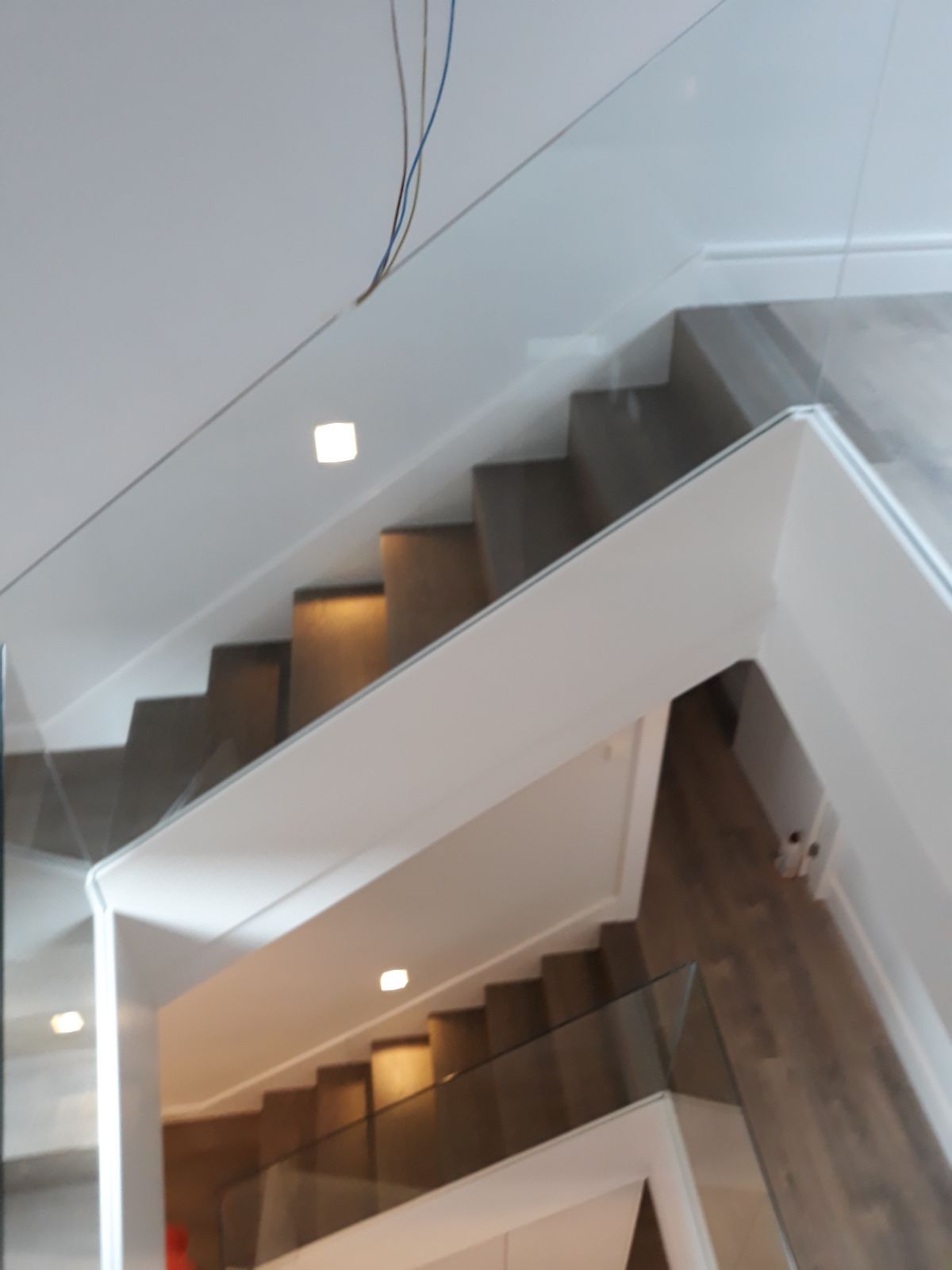 Una escalera con barandilla de cristal que sube al segundo piso.