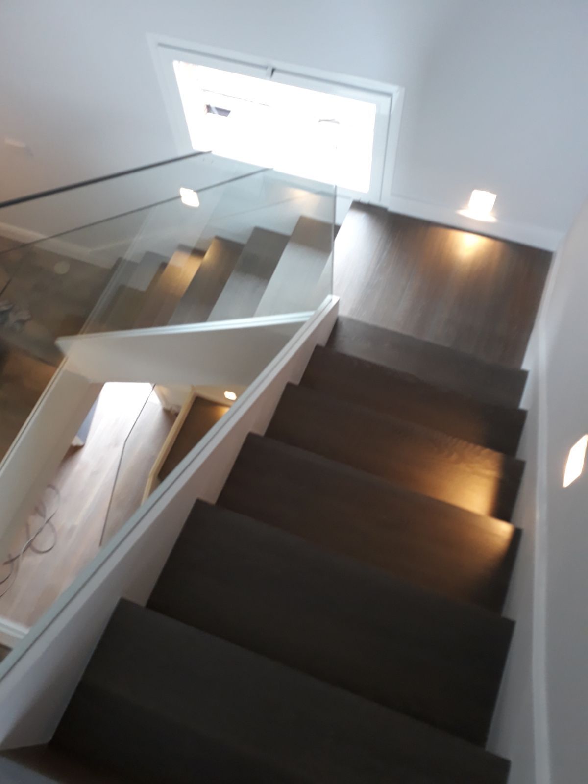 Una escalera con barandilla de cristal que sube al segundo piso.