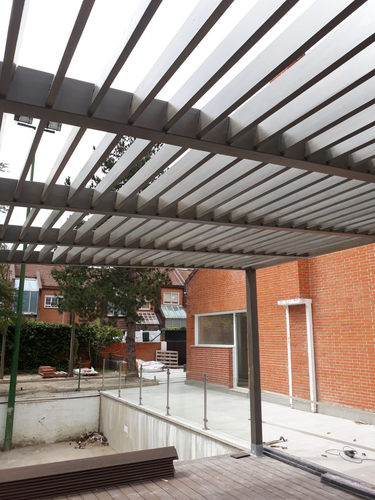 Una pérgola sobre una piscina con un edificio de ladrillo al fondo.