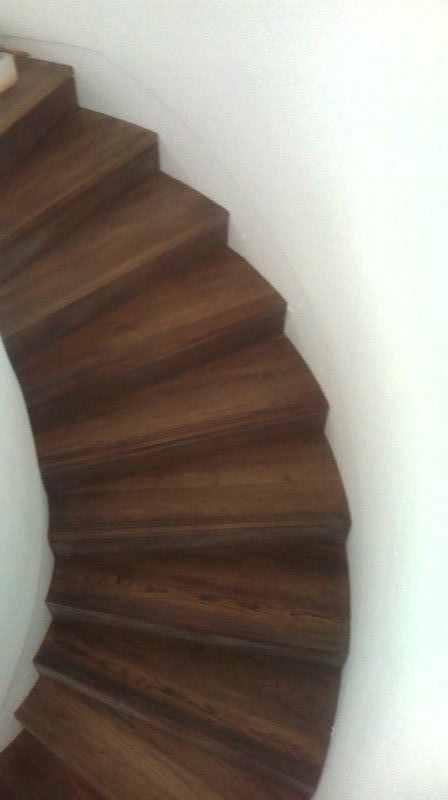 Un primer plano de una escalera de caracol de madera con una pared blanca al fondo.