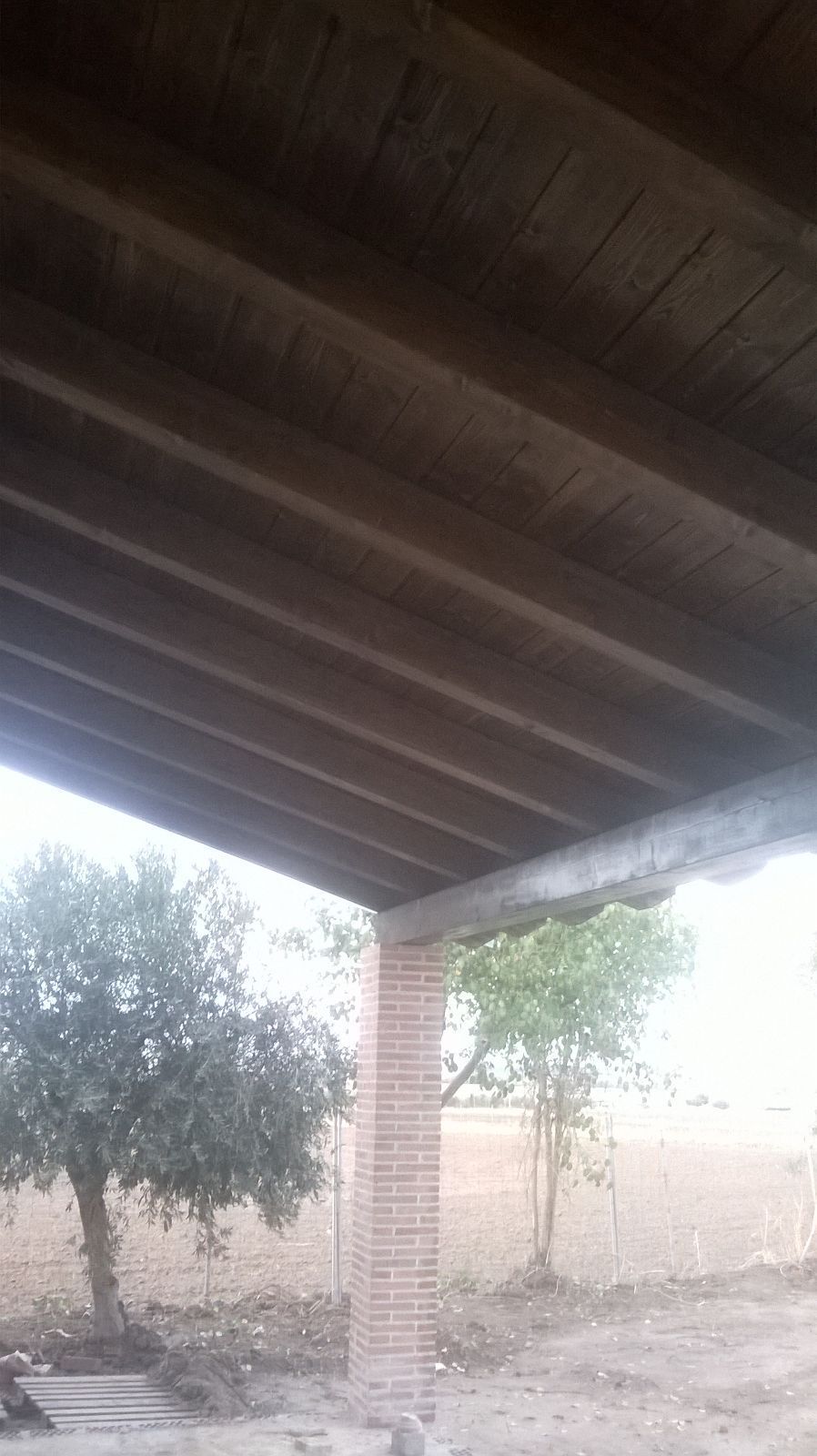 El techo de una estructura de madera con una pared de ladrillo y árboles al fondo.
