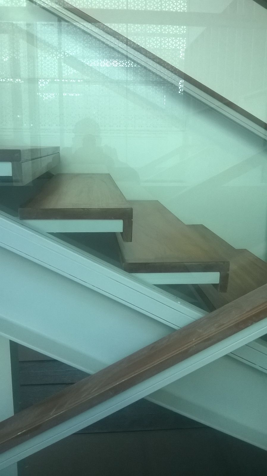 Un primer plano de una escalera con escalones de madera y barandilla de vidrio.