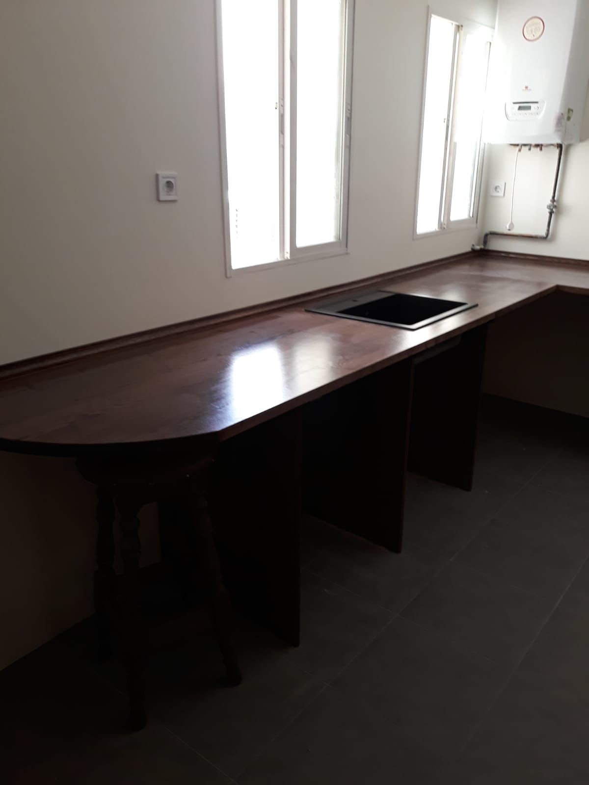 Una habitación vacía con una mesa de madera y dos ventanas.