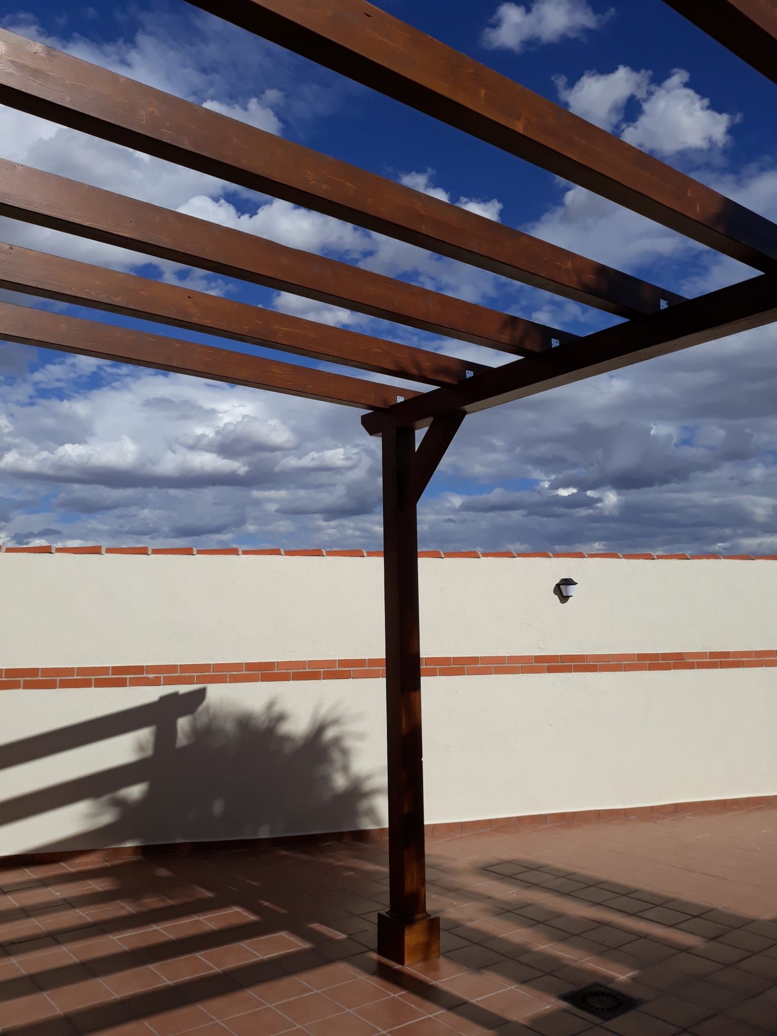 Una pérgola de madera con un cielo azul al fondo.