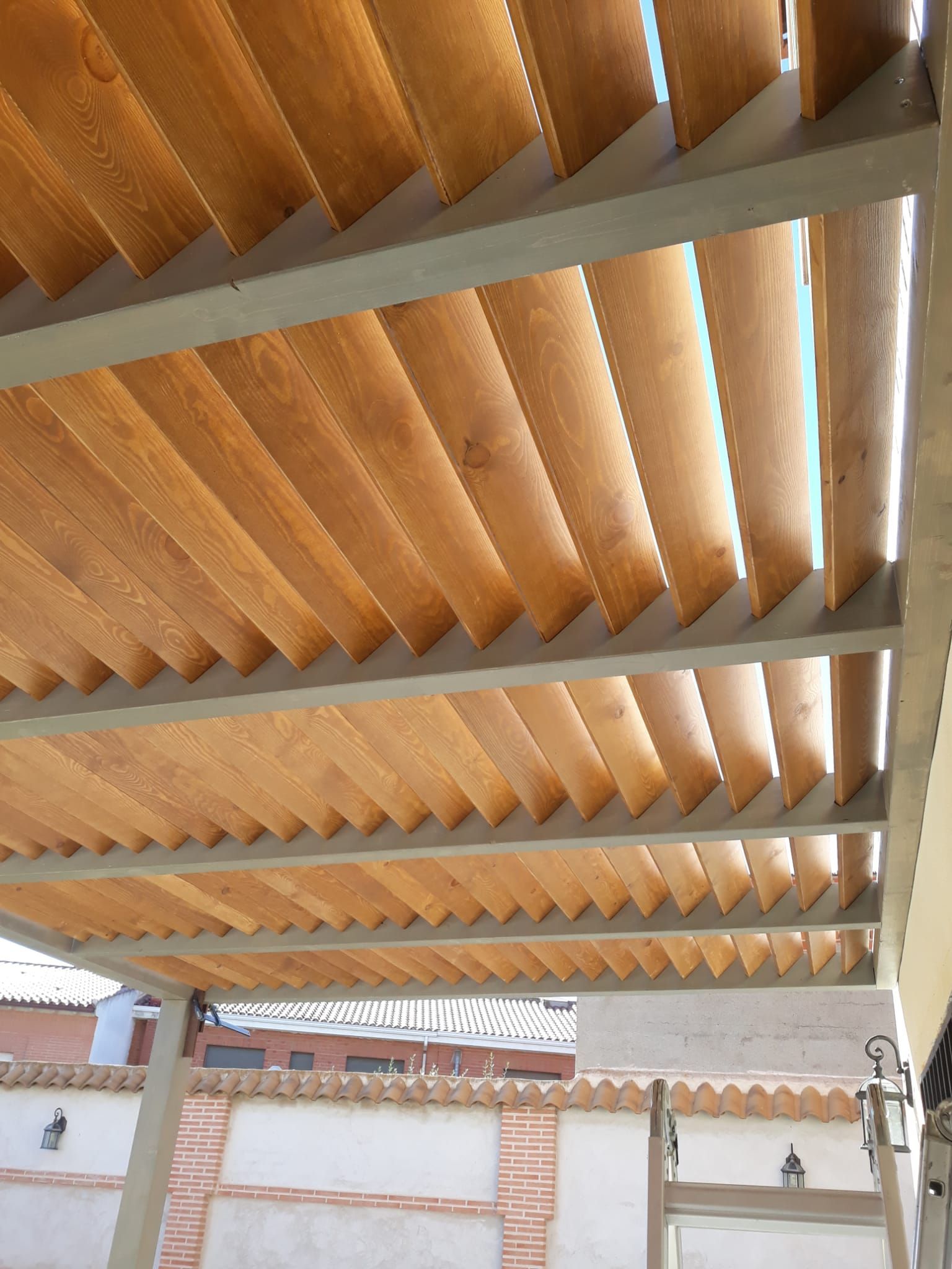 El techo de una pérgola de madera con una pared de ladrillo al fondo.