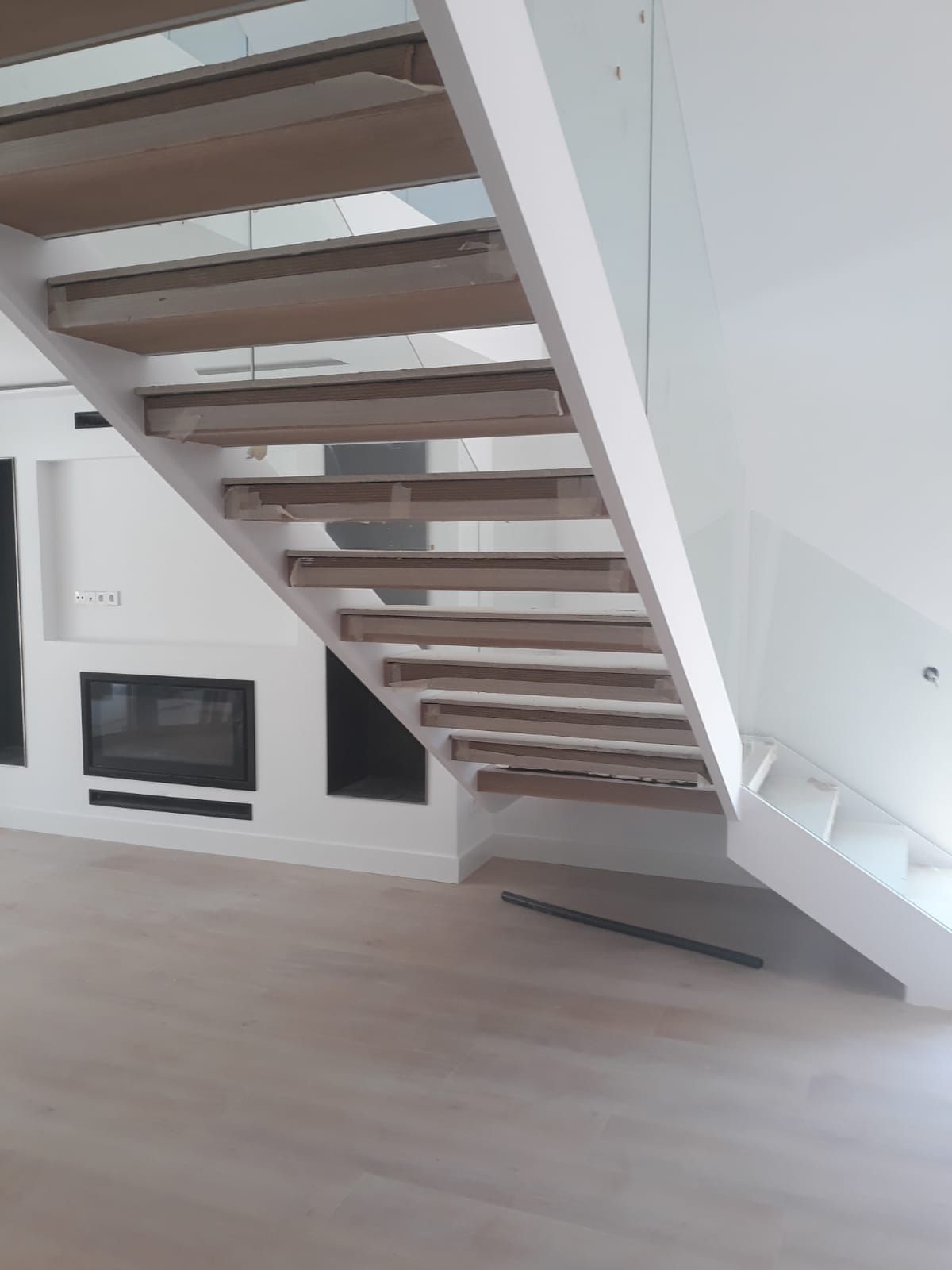 Una escalera de madera con barandilla de vidrio en una habitación vacía.