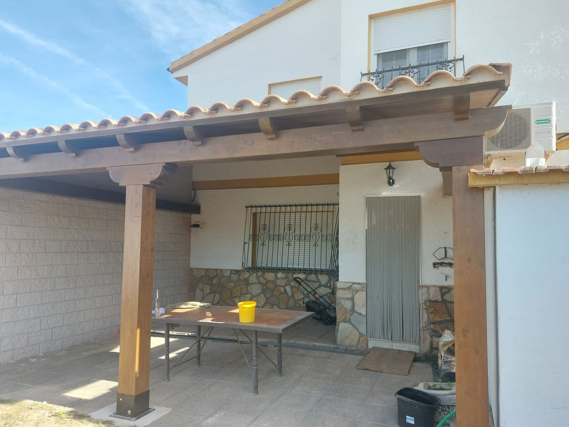 Una casa blanca con una pérgola de madera y una mesa debajo.