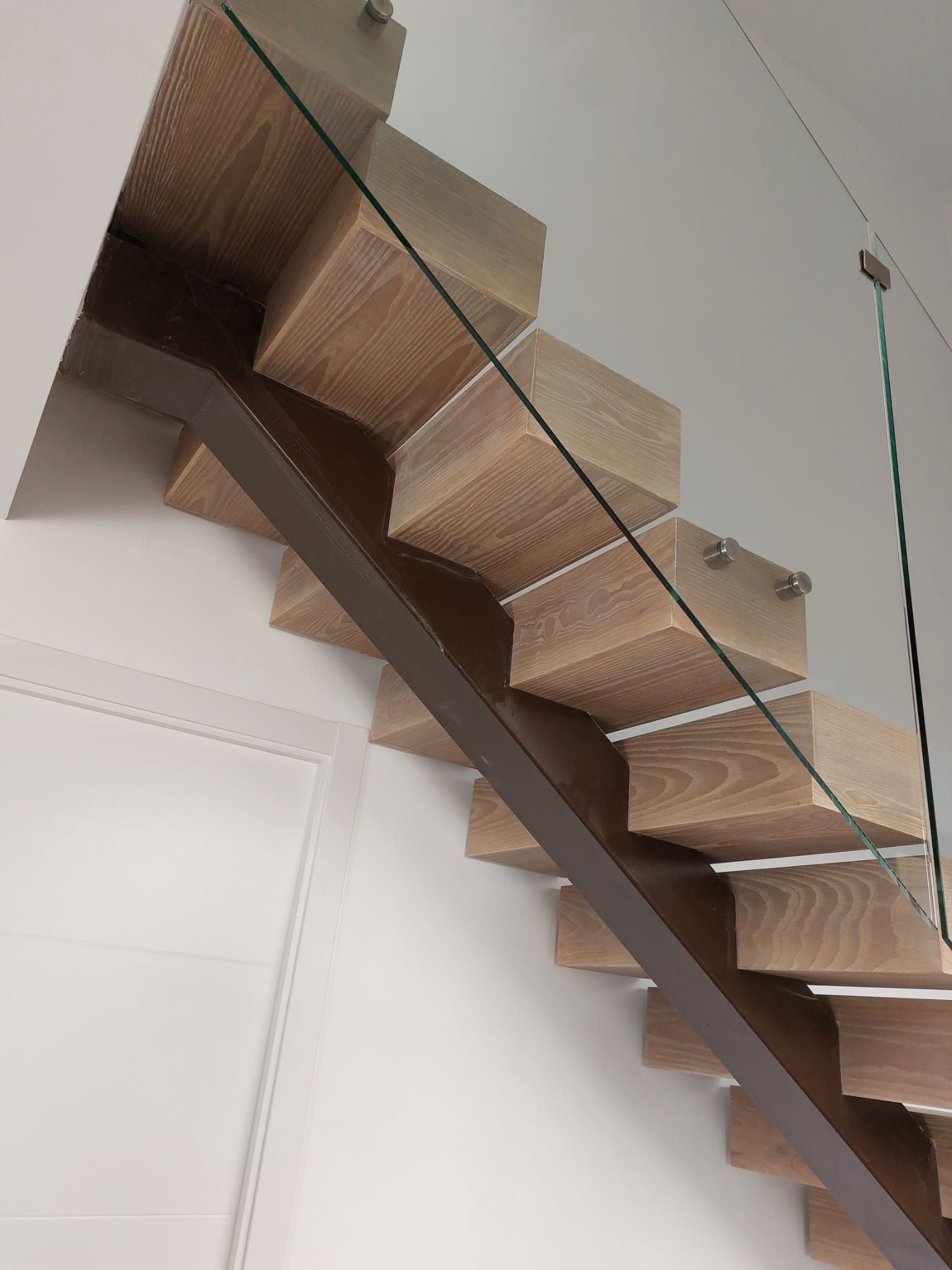 Un primer plano de una escalera de madera con barandilla de vidrio.