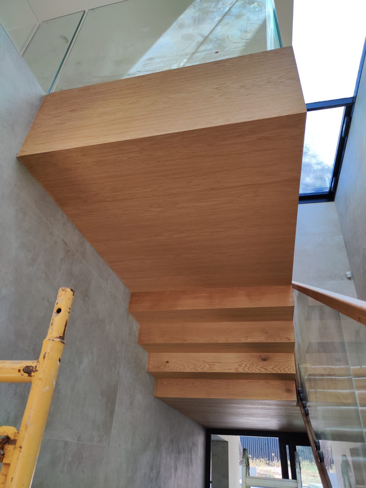 Una escalera de madera con barandilla de vidrio en un edificio en construcción.