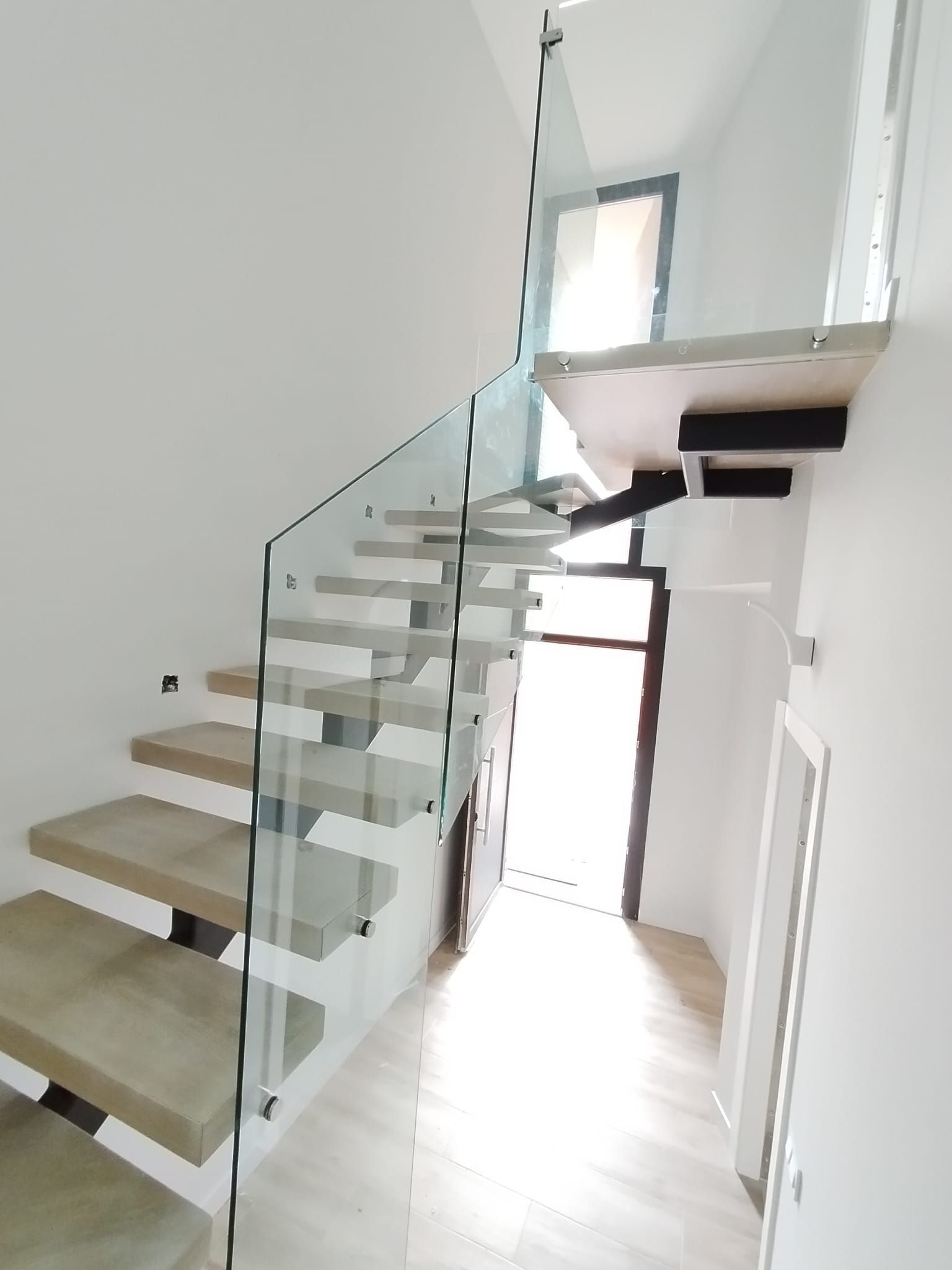 Una escalera con barandilla de cristal y escalones de madera.