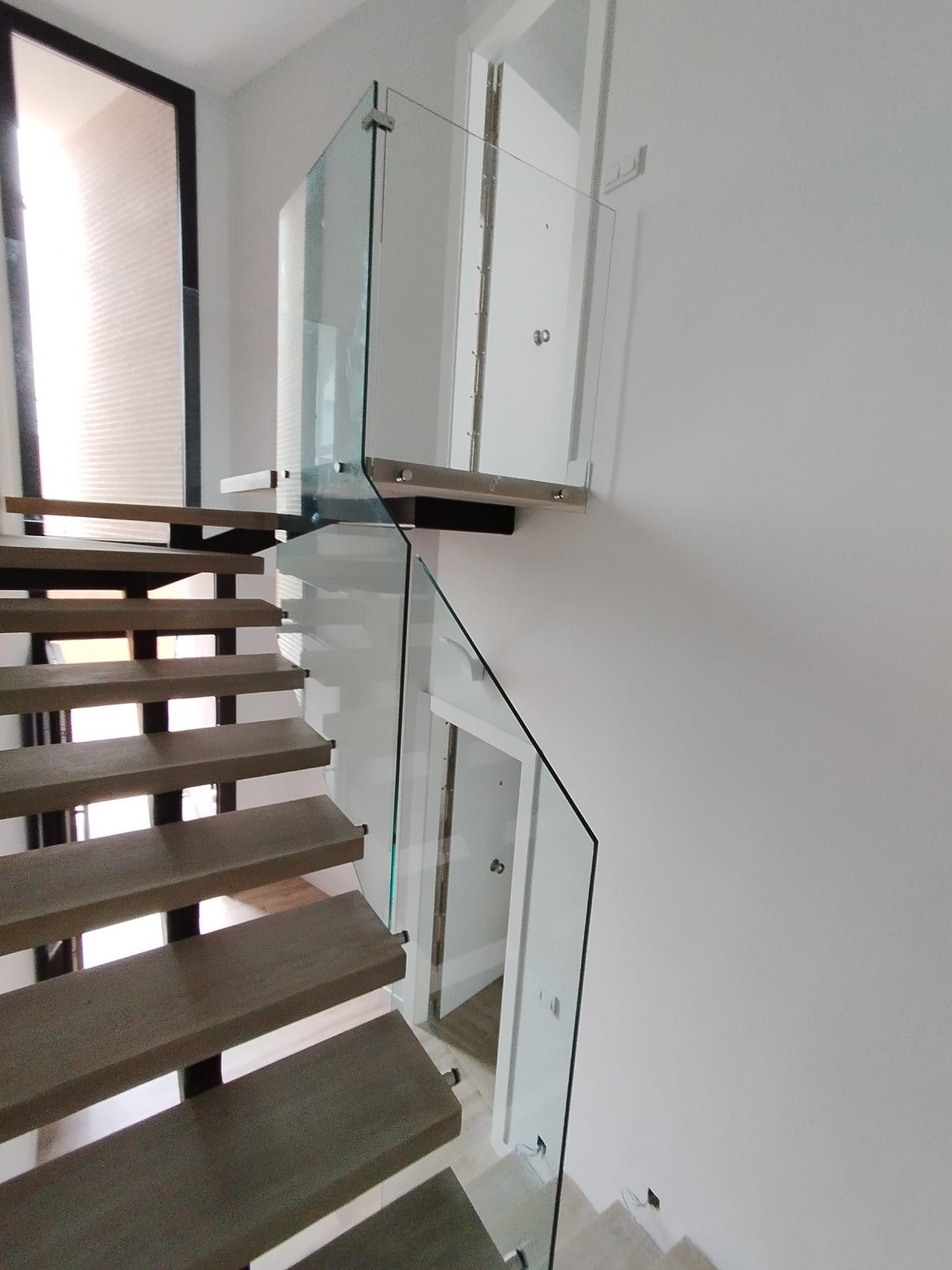 Una escalera con barandilla de cristal y escalones de madera.