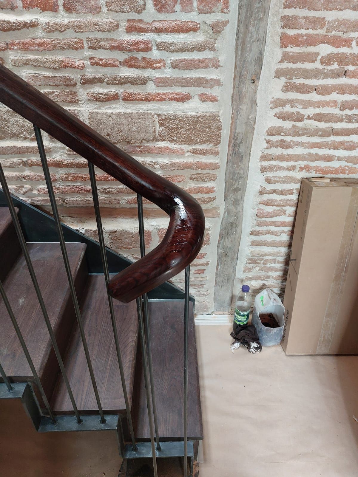 Una escalera con barandilla de madera y una pared de ladrillo detrás de ella.