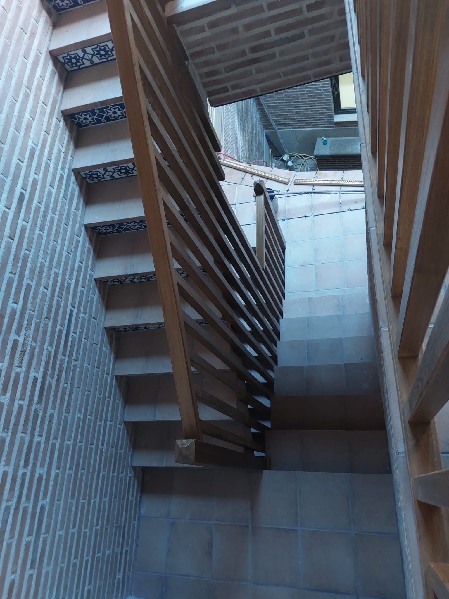 Una escalera con barandilla de madera y una pared de ladrillo.
