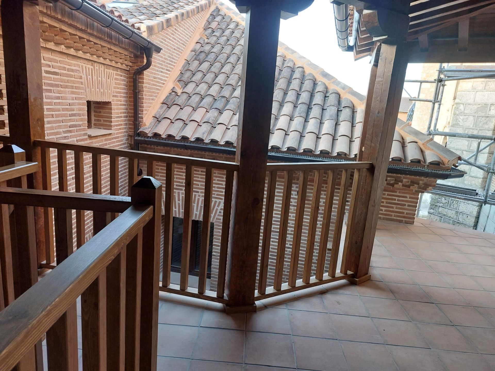 Un balcón con barandilla de madera y un edificio de ladrillo al fondo.