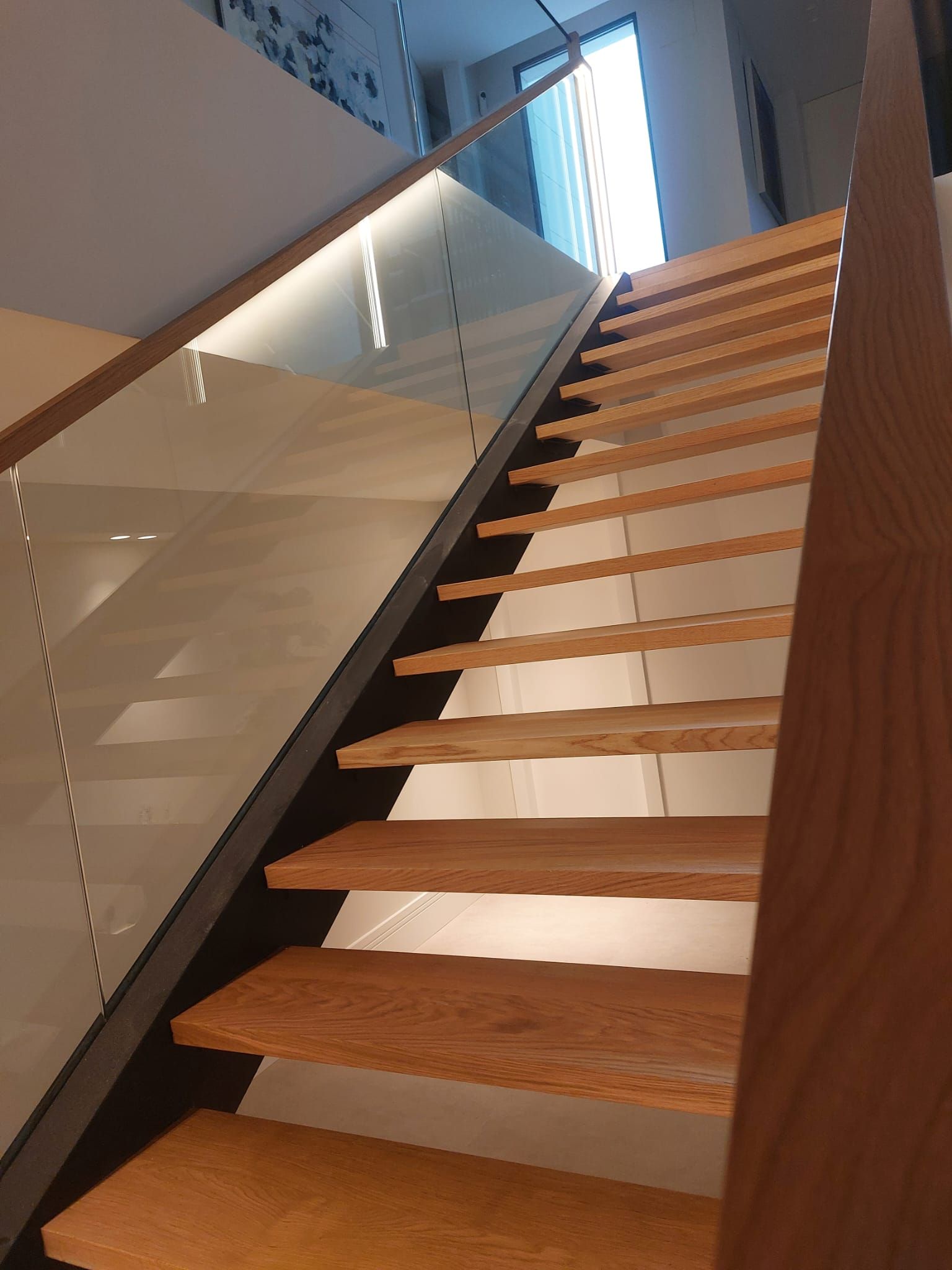 Una escalera con escalones de madera y barandilla de cristal.