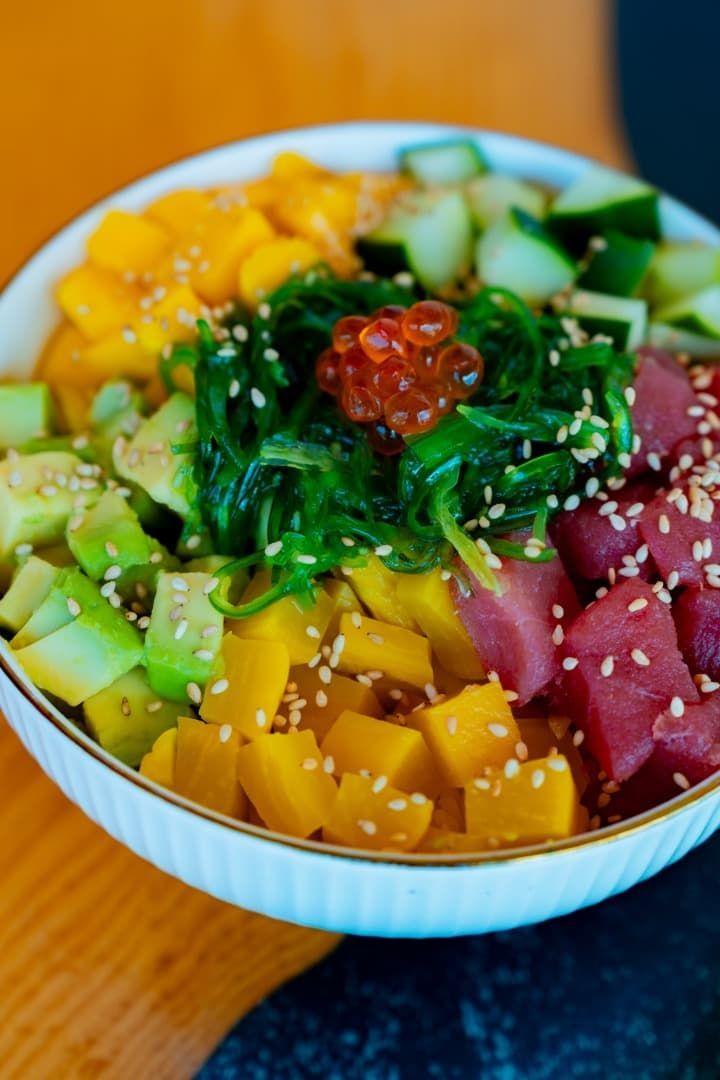 Poke bowl colorido con mango en cubos, atún, aguacate, pepino, algas, semillas de sésamo y huevas de salmón.