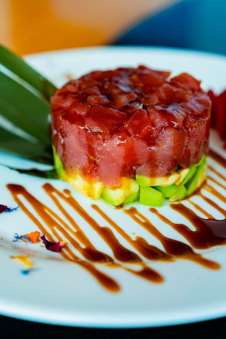 Tarta de tomate y aguacate en capas sobre un plato blanco con un chorrito de vinagre balsámico y guarnición verde.