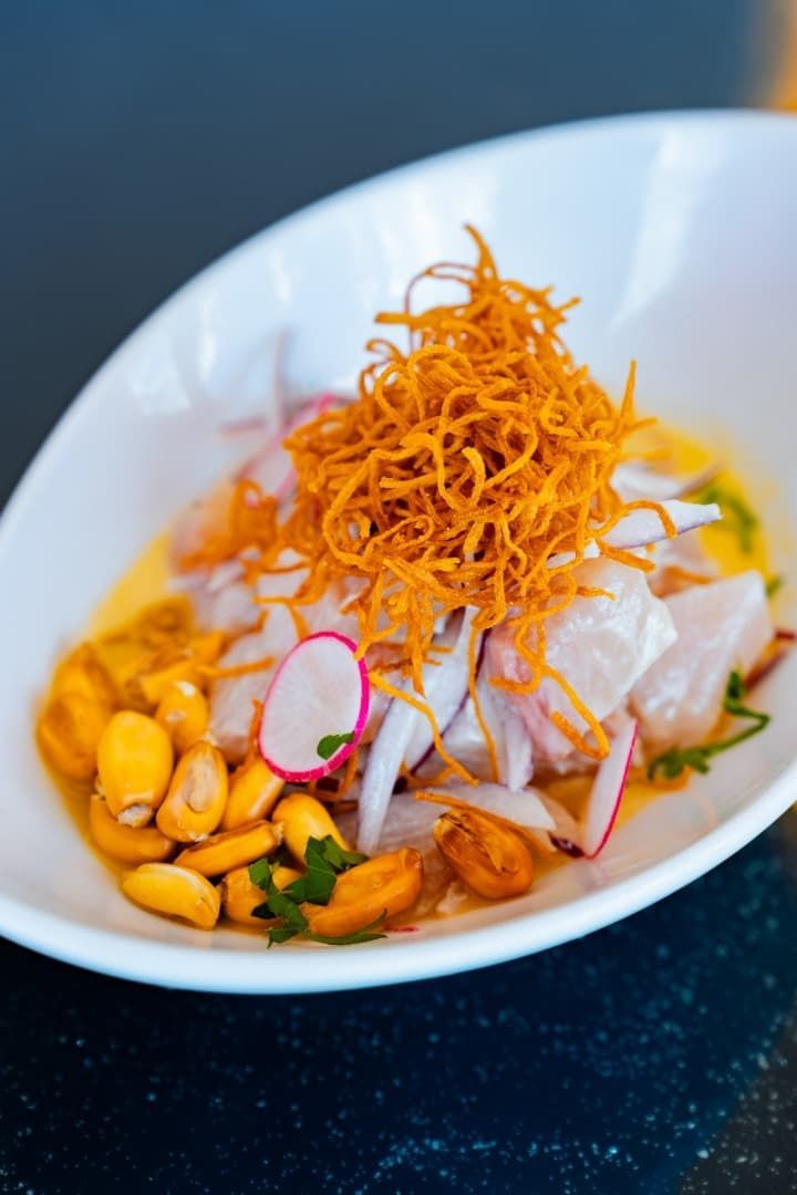 Ensalada gourmet emplatada con guarnición crujiente frita, rodajas de rábano y salsa de naranja sobre una mesa oscura.