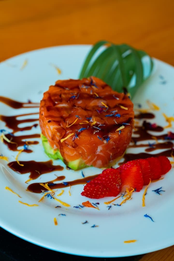 Postre glaseado con fresas y sirope de chocolate sobre un plato blanco.