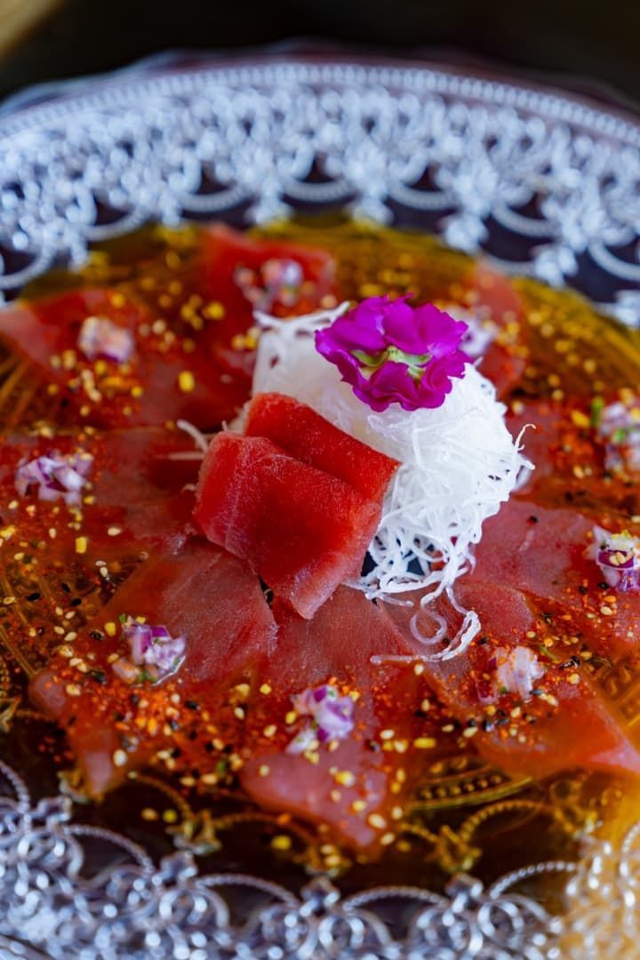 Postre de gelatina roja cubierto con fruta y azúcar hilado blanco en un plato de vidrio decorativo.