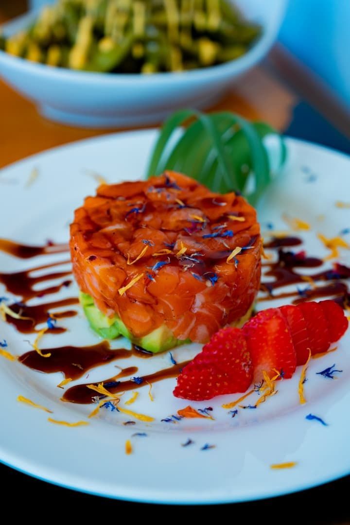 Postre de naranja glaseado en un plato blanco con sirope de chocolate y fresas, con un plato verde borroso al fondo.