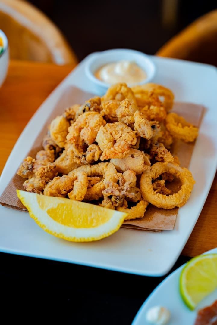 Calamares fritos en un plato blanco con rodajas de limón y salsa para mojar sobre una mesa de madera.