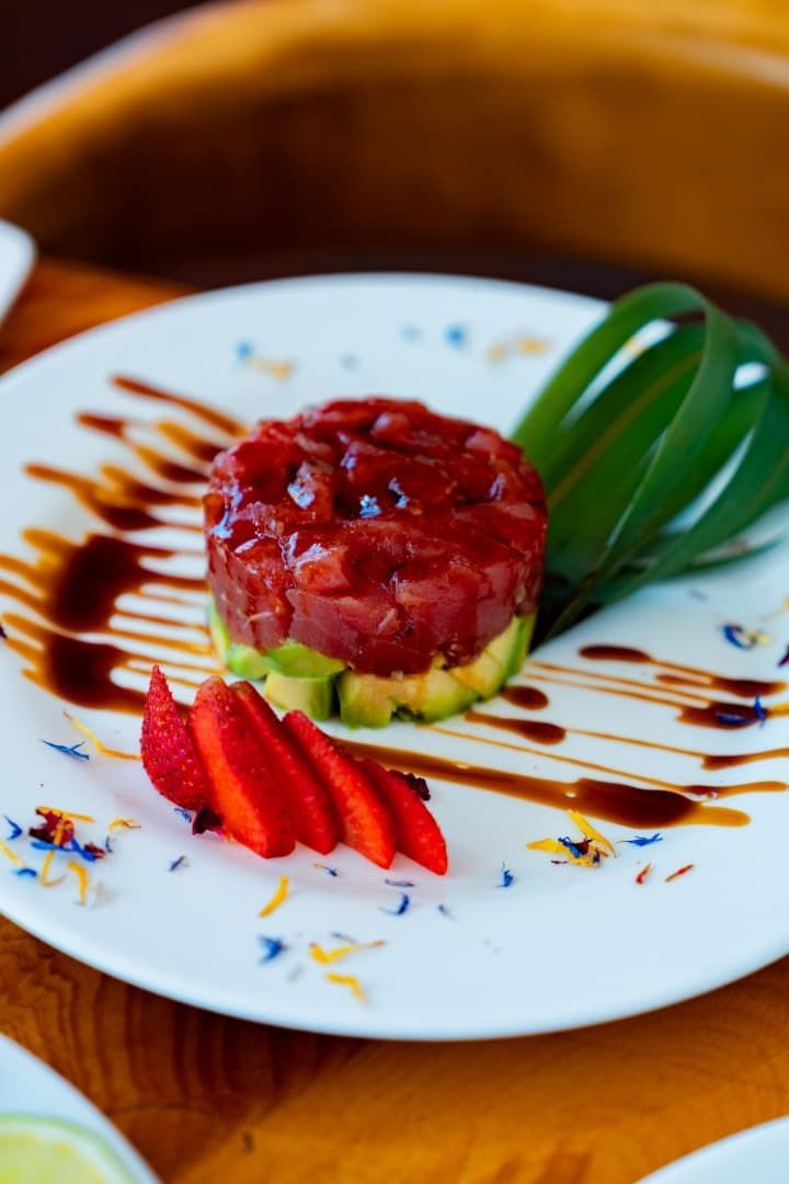 Postre de fresas emplatado con sirope de chocolate, guarnición de kiwi y fresas en rodajas sobre un plato blanco.