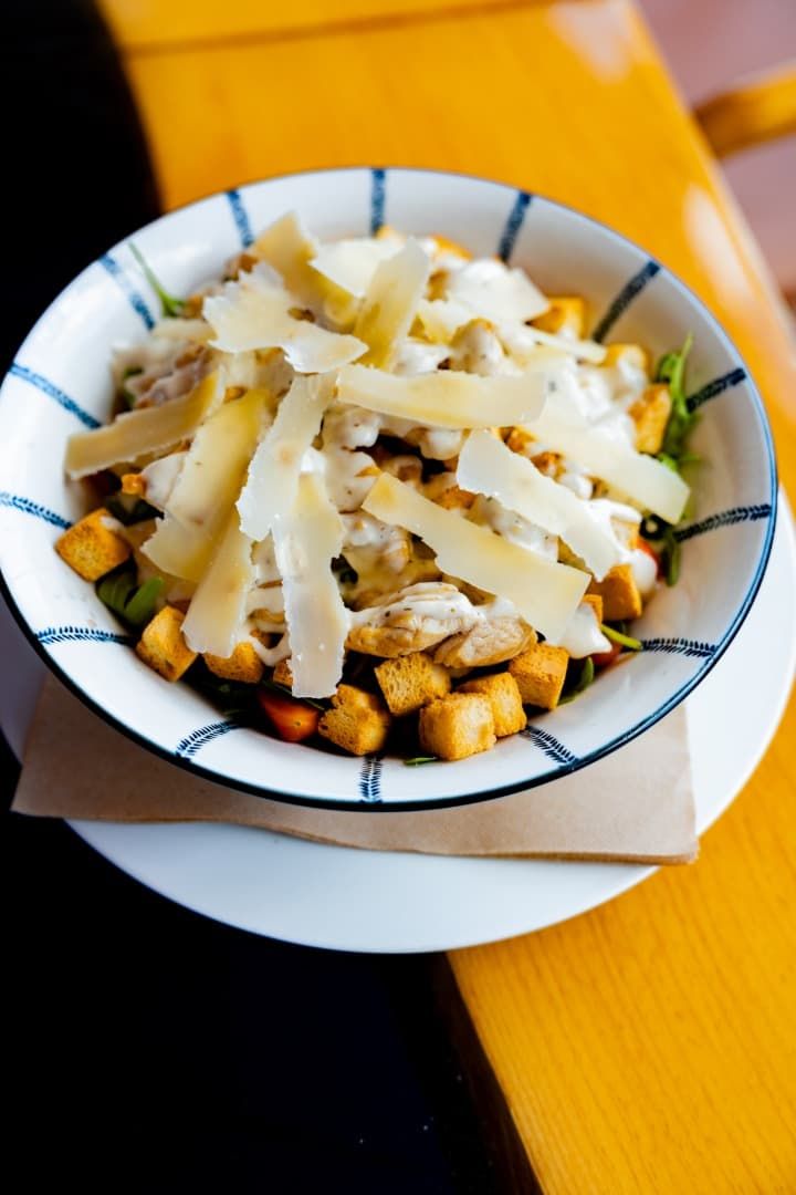 Un tazón de papas fritas cubierto con queso derretido sobre una mesa amarilla.