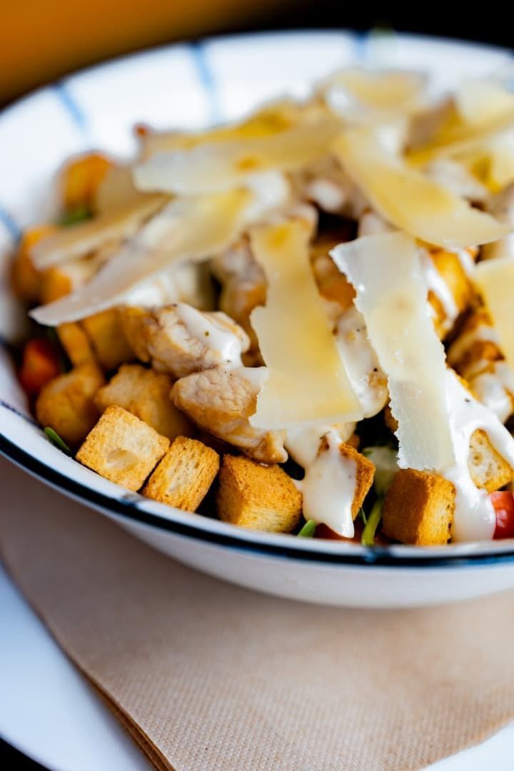 Primer plano de un tazón de ensalada cubierto con picatostes y queso rallado sobre una mesa.