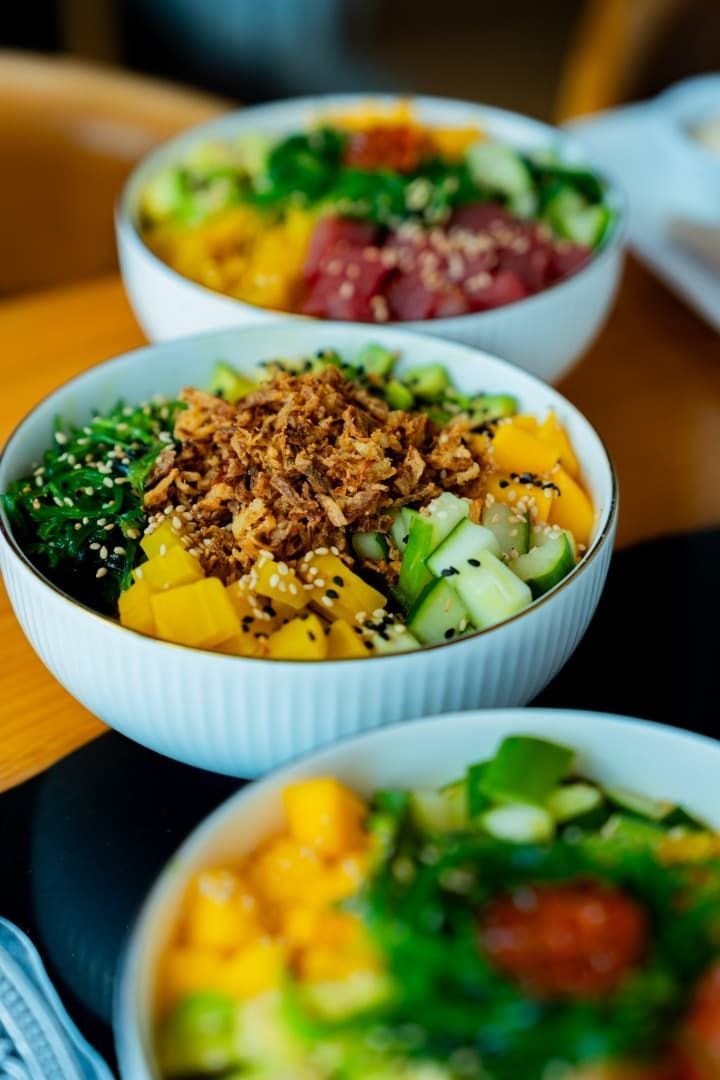 Tres coloridos cuencos de cereales cubiertos con verduras y una guarnición crujiente sobre una mesa.