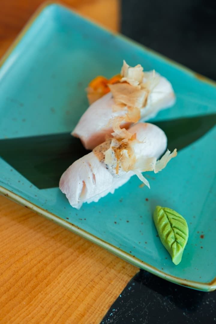 Dos rollos de sushi en un plato turquesa con una guarnición de hojas verdes sobre una mesa de madera.