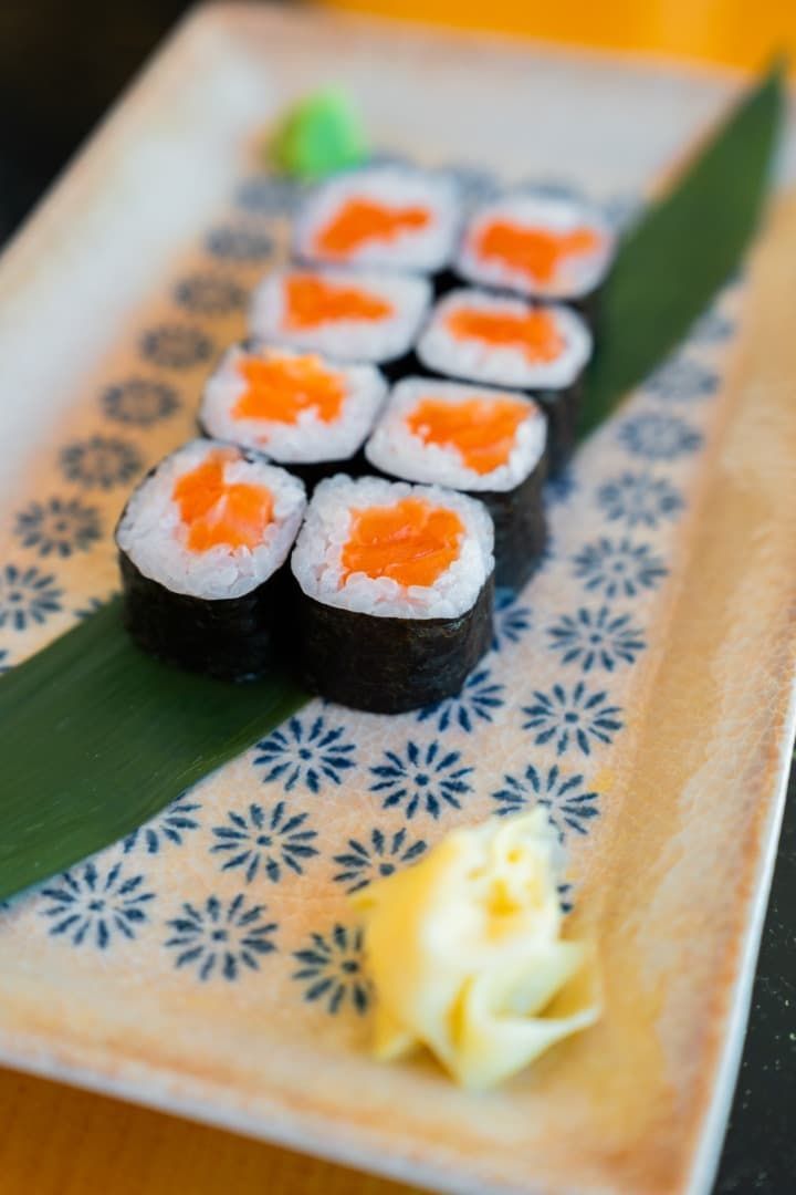 Rollitos de sushi dispuestos en un plato estampado con guarnición verde y una pequeña porción de jengibre.